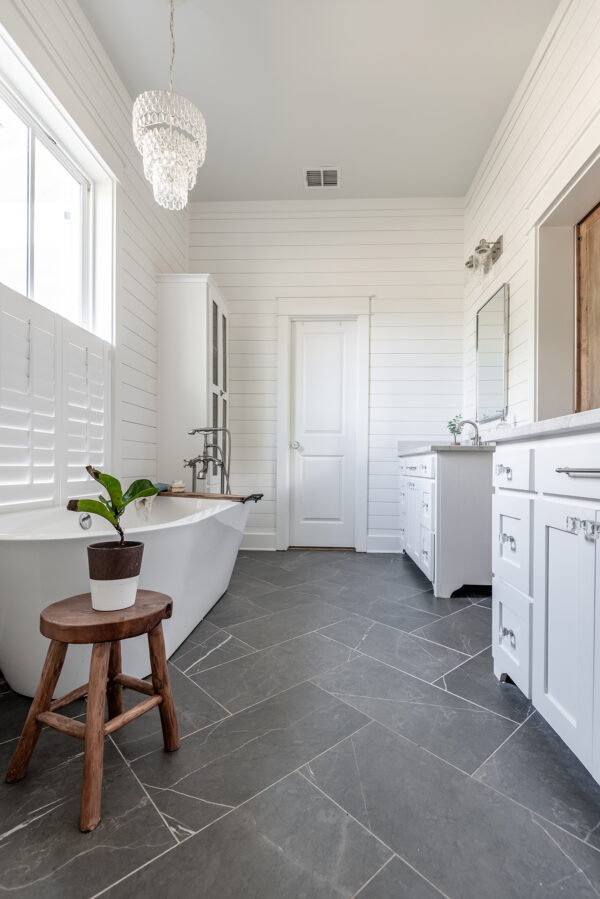 Master Bathroom with freestanding tub and shiplap walls, the floor is dark gray 12x24 tiles and there are 2 vanities and a pair of barn doors.