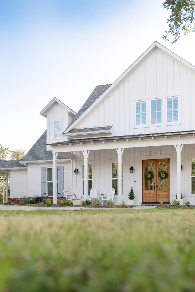 A white farmhouse with a wide front porch, a double front door, and large gable.