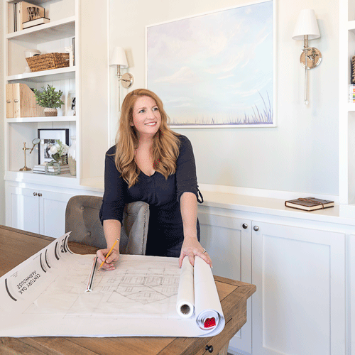 Home designer, Jessica standing at her desk looking at a set of floor plans for he Century Oak Farmhouse