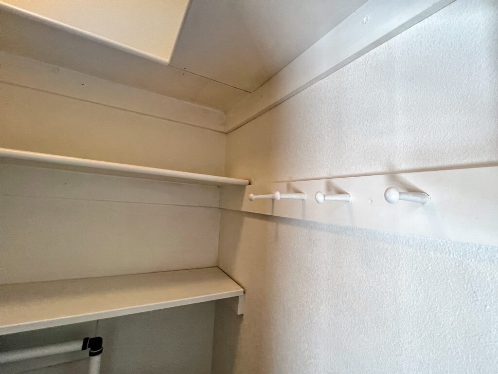 Shaker pegs pained Sherwin Williams Pure White provide hanging space for awkward items in this closet makeover.