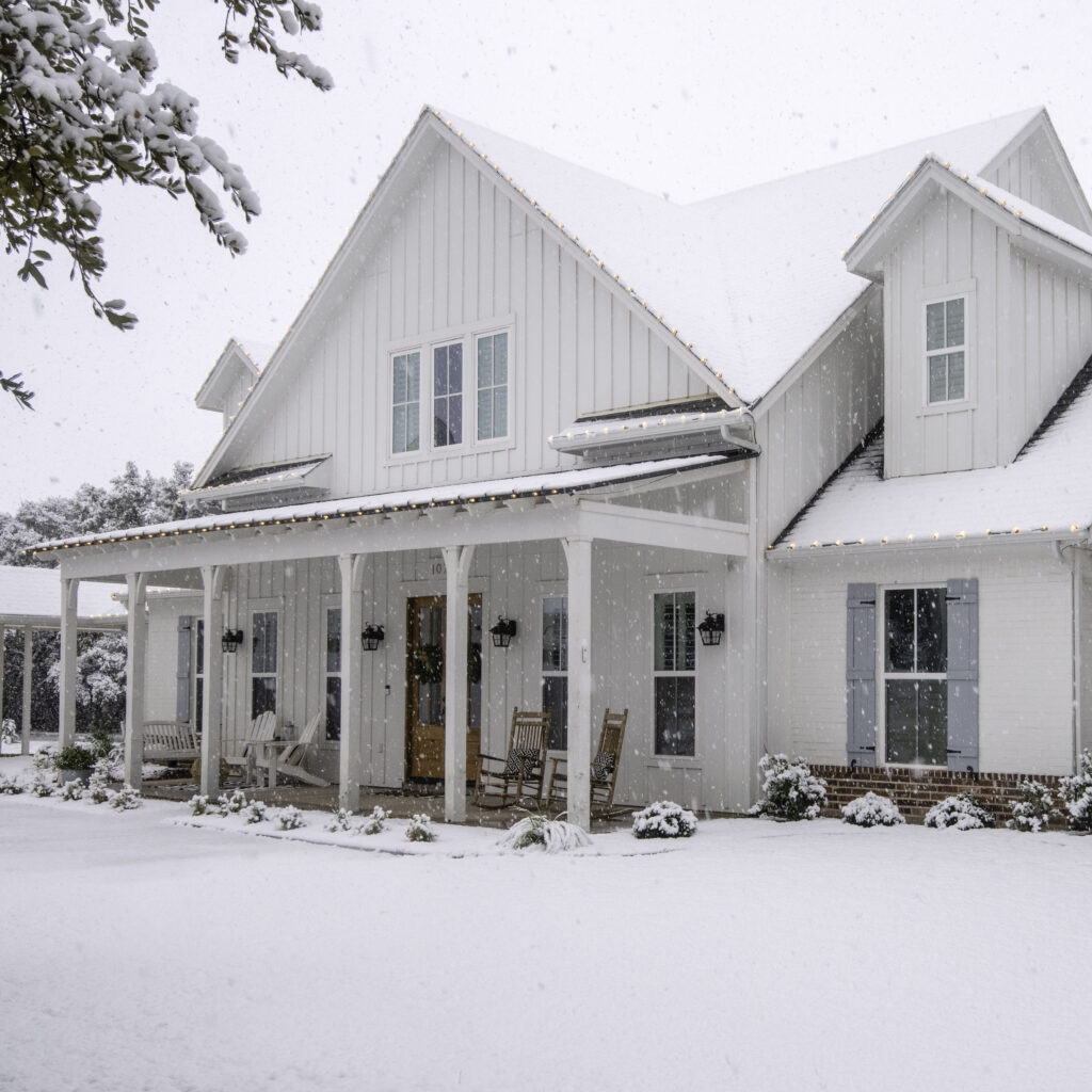 a board and batten farmhouse topped and surrounded by snow. White exterior siding