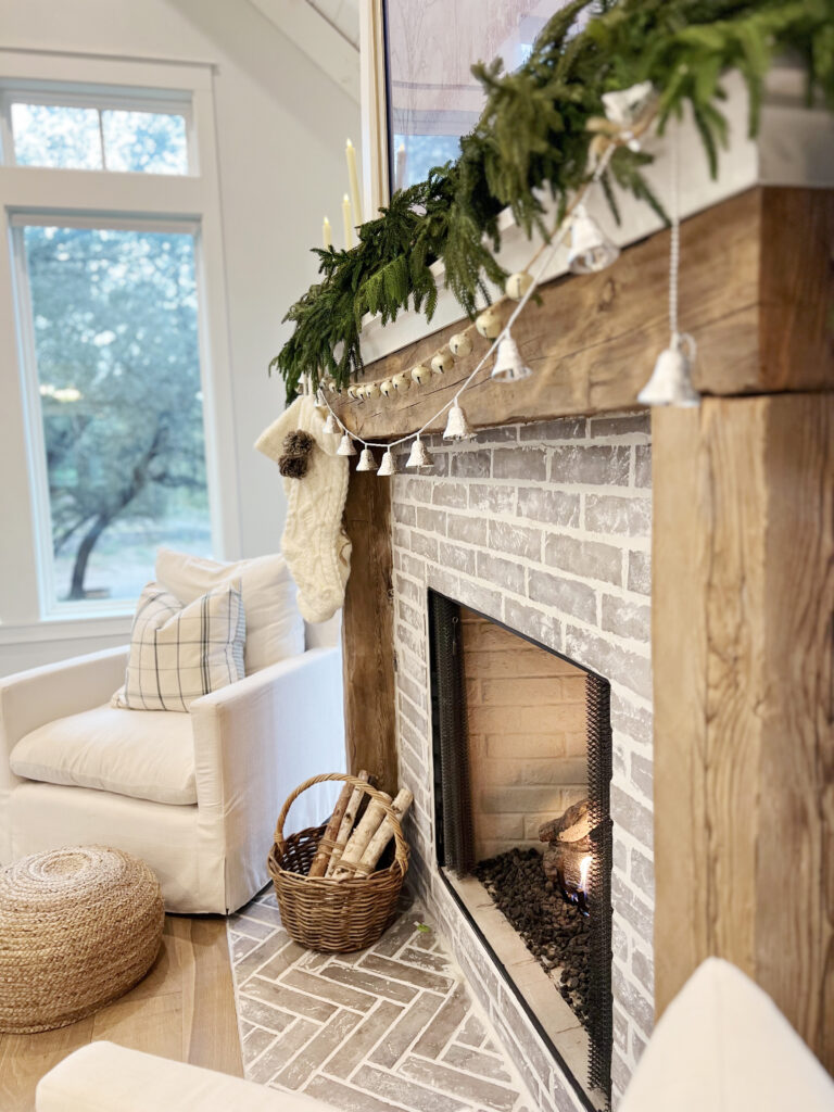 A rustic reclaimed wood mantel holds a mix of garlands, and2 strands of bells drape below.