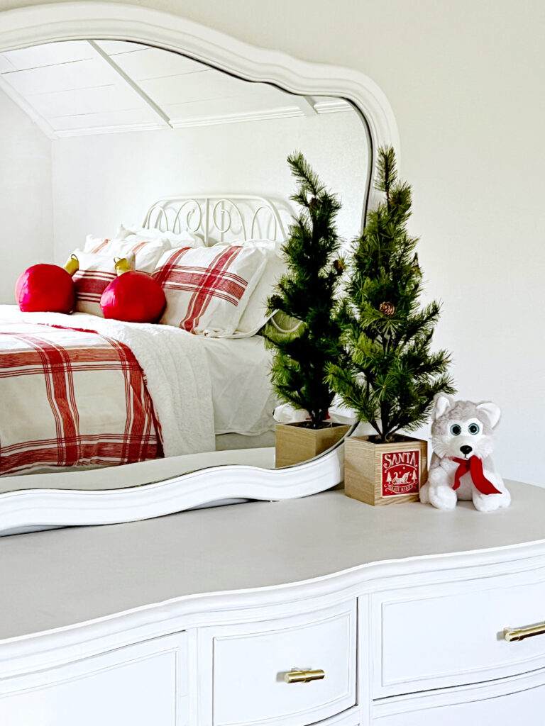 a girls bedroom decorated in red and white for Christmas with a red and white plaid blanket and red ornament ball pillows