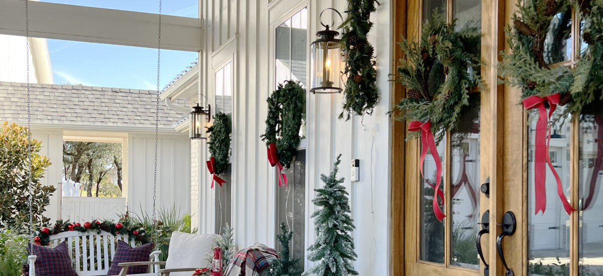 Christmas front porch with wreaths on the windows and small lighted Christmas trees