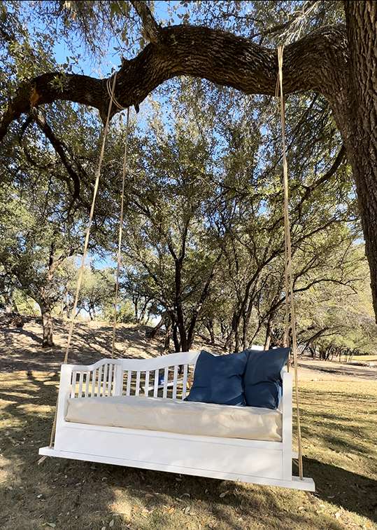 A bed swing made from a toddler bed hangs from a tree branch